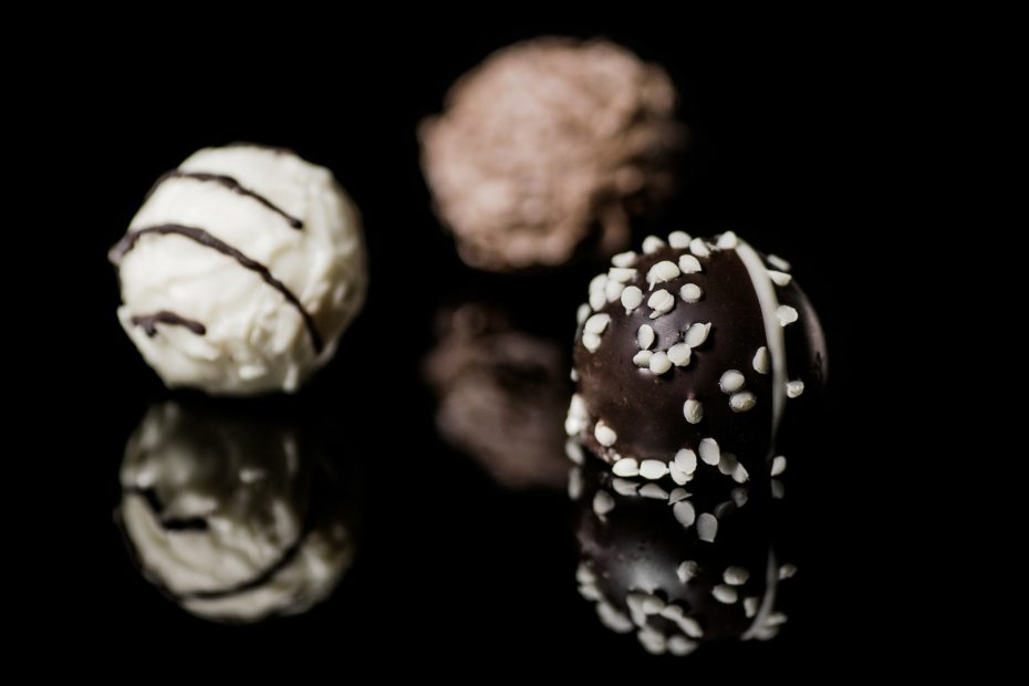 Round chocolate truffles: One white with dark chocolate drizzle, one dark chocolate with salt or sesame seeds, we're not sure which, an done milk chocolate kind of fuzzy in the background.